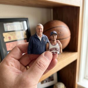 Miniature basketball keepsake figurine of grandfather and grandson displayed in hand beside basketball memorabilia.